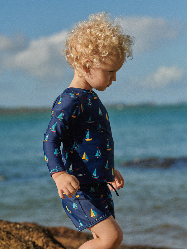 Child wearing a navy swimsuit with sailboat pattern made with ECONYL® Regenerated Nylon on a beach